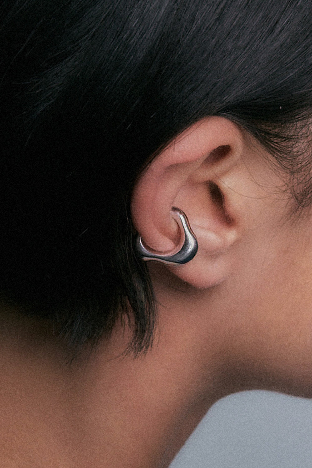 A close-up side profile of a person's ear wearing a polished silver-toned curved hoop earring.