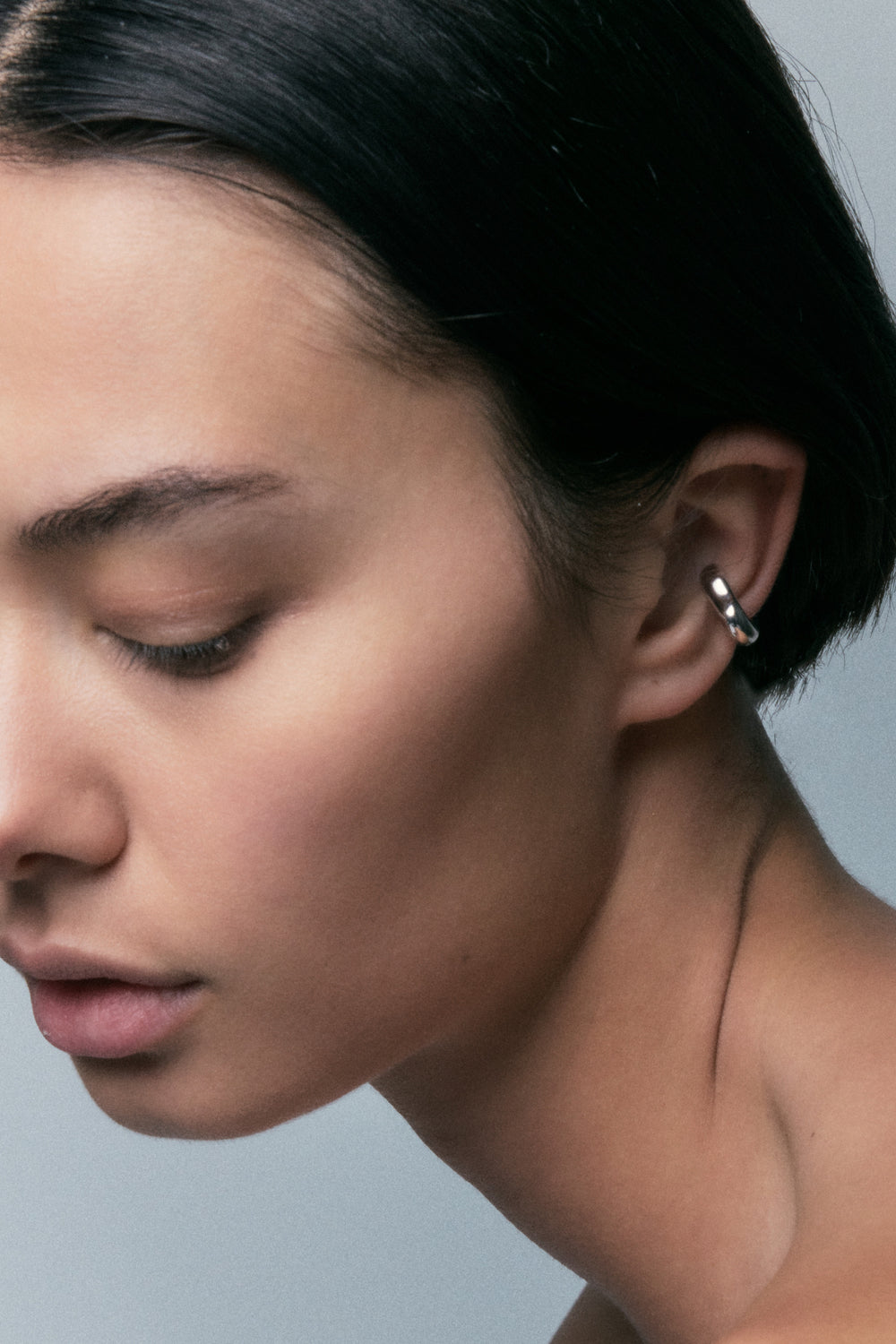 FF Ear Cuff in 925 silver, a slim polished band on the ear rim, head turned down.
