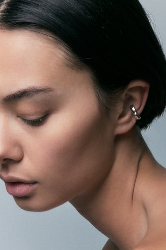 FF Ear Cuff in 925 silver, a slim polished band on the ear rim, head turned down.
