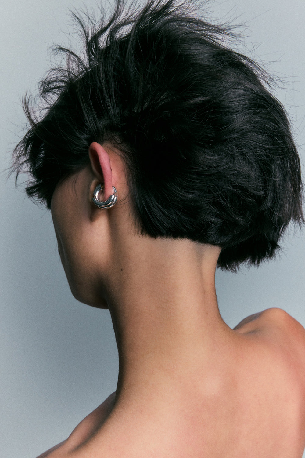Polished silver hoop worn on the earlobe, viewed from behind.