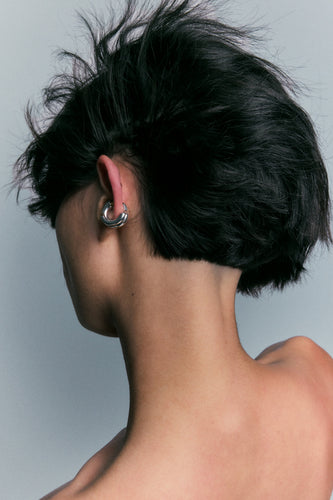 Polished silver hoop worn on the earlobe, viewed from behind.